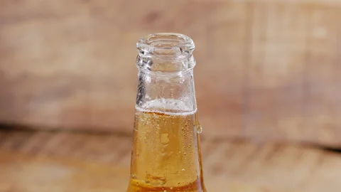 Man's hand putting a beer bottle on a wooden table with a small splash. Stock Footage 342396247