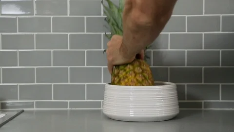 Man's hand putting pineapple and banana into a white bowl against a blue tile Stock Footage 115329172