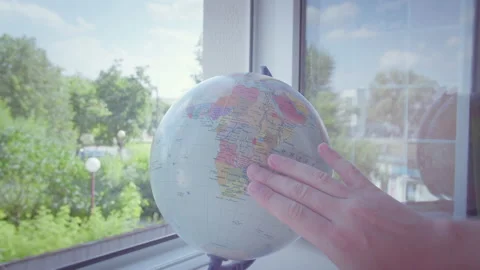 The man's hand rotates the globe, which stands on the windowsill by the open Stock Footage 167028657