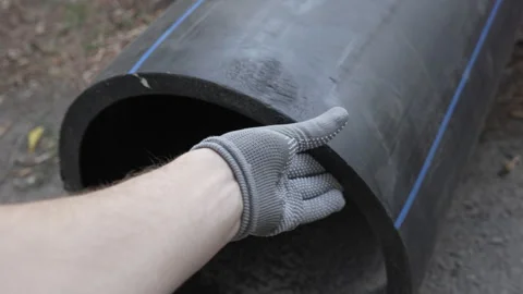 A man's hand runs along the edge of a large diameter black plastic pipe Stock Footage 287686553
