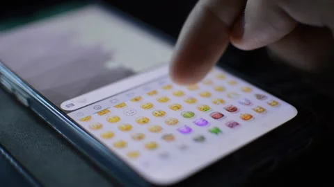 Man's hand scrolling cute yellow face emoticon on the keyboard of the phone. 库存影片 219467578