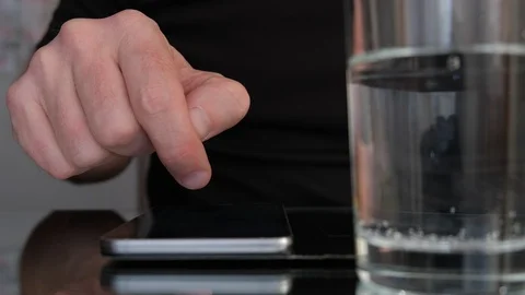 Man's hand scrolling on a smartphone next to a glass of water. Slow motion. Stock Footage 105419043