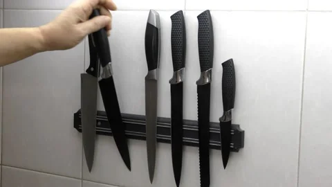 The man's hand selects the desired item from a set of knives on a magnetic strip Stock-Footage 149144589