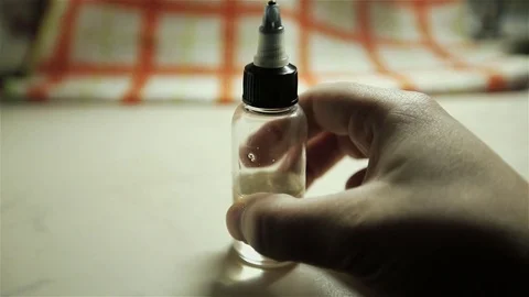 Man's hand shakes a bottle with liquid and flavor for electonic cigarette Stock Footage 72414799