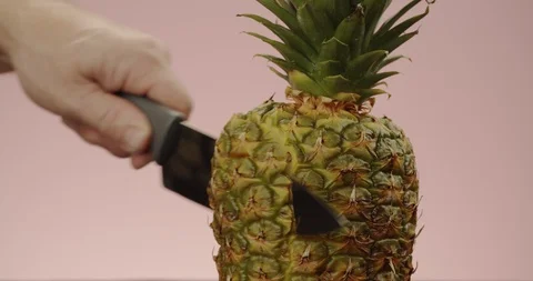 Man's hand with sharp knife cuts off slice from whole pineapple. 4K Slow Motion Stock Footage 125066747