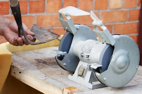 Mans hand sharpens a hoe on electric grindstone in rural shed Stock Photos
