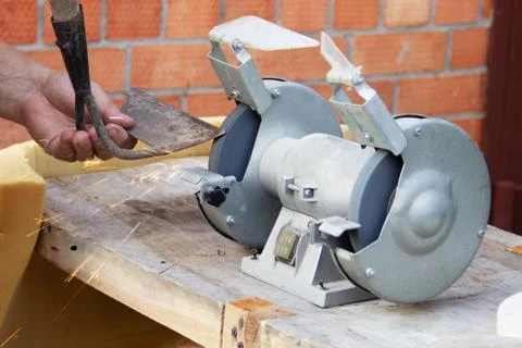 Mans hand sharpens a hoe on electric grindstone in rural shed Stock Photos