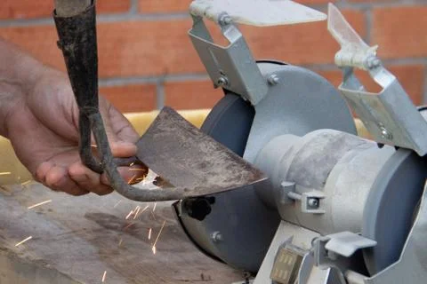 Mans hand sharpens a hoe on electric grindstone in rural shed Stock Photos