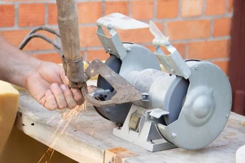 Mans hand sharpens a hoe on electric grindstone in rural shed Stock Photos