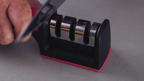 A man's hand sharpens a kitchen knife in a special sharpener on the table 库存影片 246427930