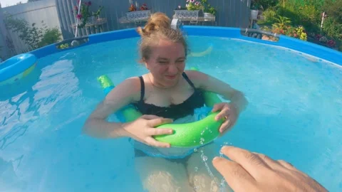 A man's hand splashes in the face of a plump woman who is swimming in pool Stock Footage 201645204