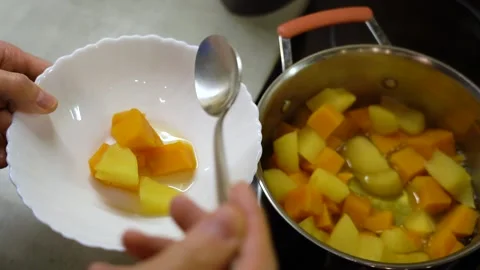 Man's hand spoons boiled pumpkin and apples from pan into white bowl 库存影片 232892913