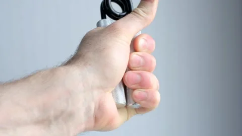 A mans hand squeezes and unclenched an expander to strengthen his grip on a gray Stock Footage 336775389