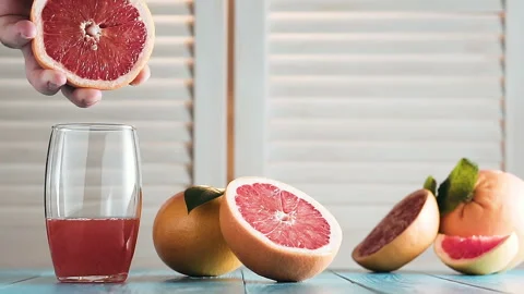 Man's hand squeezes juice from a grapefruit into a glass. Video stock 87346372