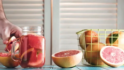 Man's hand squeezes juice from grapefruit into mason jar and inserts straw. Stock Footage 87387755