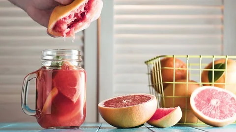 Man's hand squeezes juice into mason jar and throws out squeezed grapefruit. Video stock 87348232