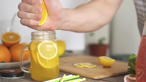 A man's hand squeezes the juice from an orange into a glass. Man holds half Stock Footage 155941101
