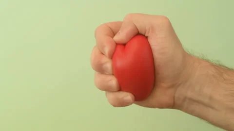 Man's hand squeezes red anti-stress heart toy on a green background Stock Footage 147367617