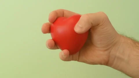 Man's hand squeezes red anti-stress heart toy on a green background Stock Footage 147367659