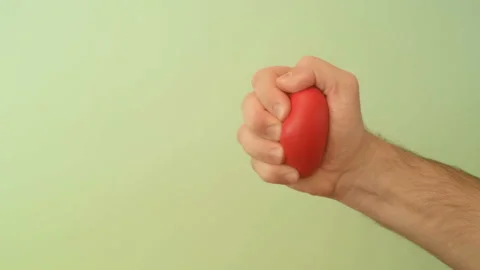 Man's hand squeezes red anti-stress heart toy on a green background Stock Footage 147367726