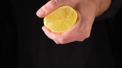 Mans hand squeezing lemon juice from a half lemon on dark background Stock Footage 150171151