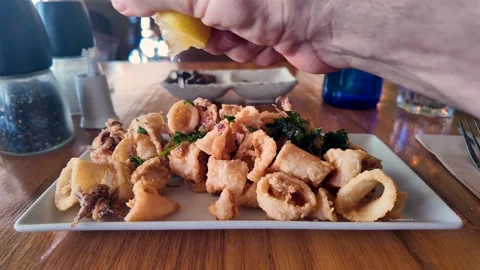 A Man’s Hand Squeezing a Lemon Over a Plate of Andalusian-style Calamari. Slow Video stock 328977173