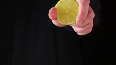 Mans hand squeezing lime juice from a half lemon on dark background Stock Footage 150171159