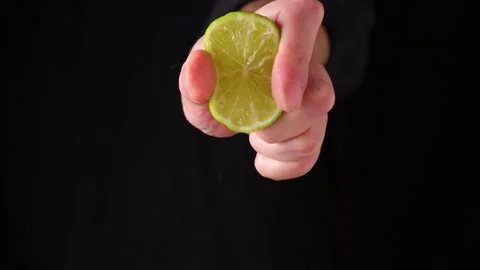 Mans hand squeezing lime juice from a half lemon on dark background Stock Footage 150171259