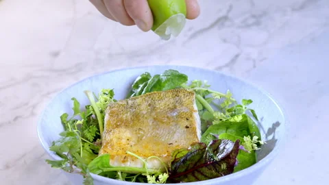 Man's hand squeezing lime juice on white fish, pike-perch zander and salad. Stock Footage 274463170