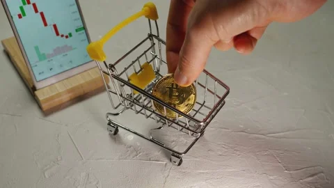 A man's hand stacking Bitcoin cryptocurrency gold coins in a shopping cart Stock Footage 169030228