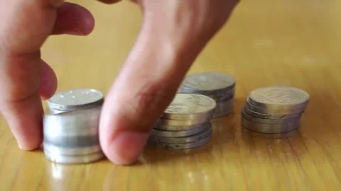 A man's hand stacking piles of Indonesian Rupiah coins on a wooden office desk. Stock Footage 322144536