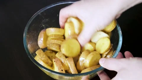 A man's hand stirs potatoes marinated in spices for baking in a glass bowl. Stock Footage 233270628