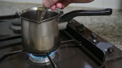 A man's hand stirs with a spoon inside a coffee warmer pan. Stock Footage 257374498
