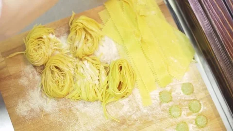 Man's hand strew with flour different kinds of pasta, ravioli, spaghetti, on the Stock Footage 74532301