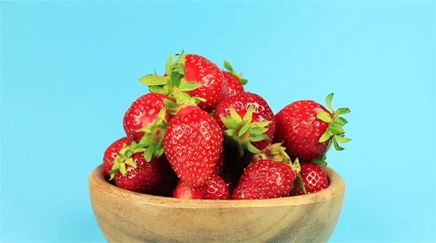 Man's hand take red ripe strawberry in wooden bowl on blue background Stock Footage 63867853