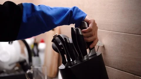 Man's hand takes large kitchen knife and set of knives standing in kitchen 库存影片 233539519