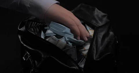 A man's hand takes stacks of dollars from a leather bag on a black background. A Stock Footage 273031412