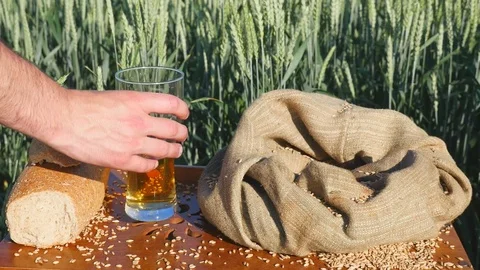 Man's hand taking a bottle of cold beer and a piece of bread on wheat background Video stock 77160849