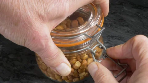 Man’s hand taking a handful of raw peanuts from a glass storage jar. Stock Footage 145579667