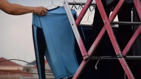 Man's hand taking simple clothes from steel drying rack on rooftop in Indones Stock Footage 312057428