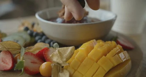 Man's hand throws blueberries on wooden plate with fruit mix Stock Footage 103802799