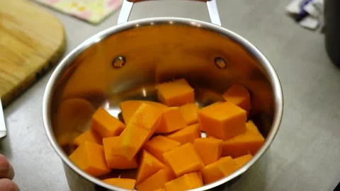Man's hand throws cut pumpkin cubes into cooking pot Vidéo 232780178
