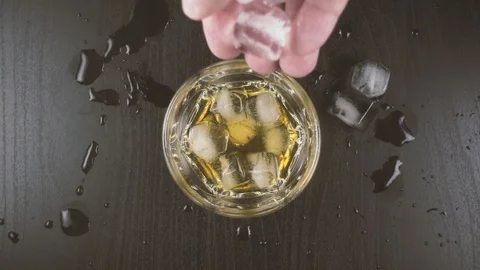 Man's hand throws ice into a glass of whiskey Stock Footage 87652299