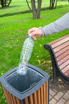 A man's hand throws a plastic bottle into a trash can. Stock Photos