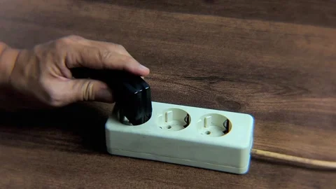 A man's hand tries to plug a black charger adapter into an electrical outlet. Stock-Footage 338447586