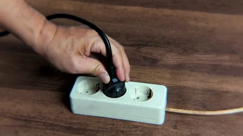 A man's hand tries to plug a black power cord into an electrical socket. Stock-Footage 338448003
