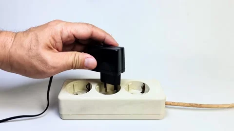 A man's hand tries to plug a black charger adapter into an electrical socke.. Stock-Footage 338488435