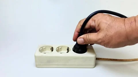 A man's hand tries to plug a black power cord into an electrical socket on .. Stock Footage 338579344