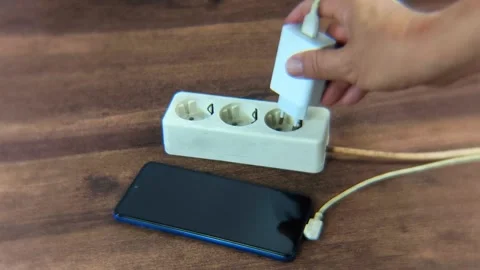 A man's hand trying to plug a cell phone charger into an electrical outlet .. Stock-Footage 338447713
