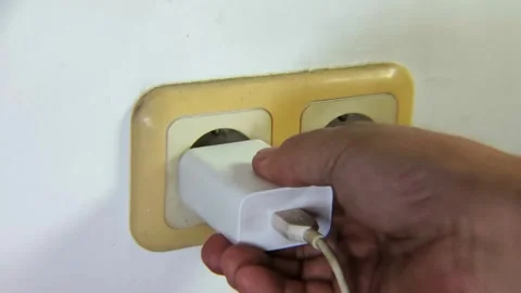 Man's hand trying to plug a cell phone charger to the electrical socket. Stock Footage 338447995